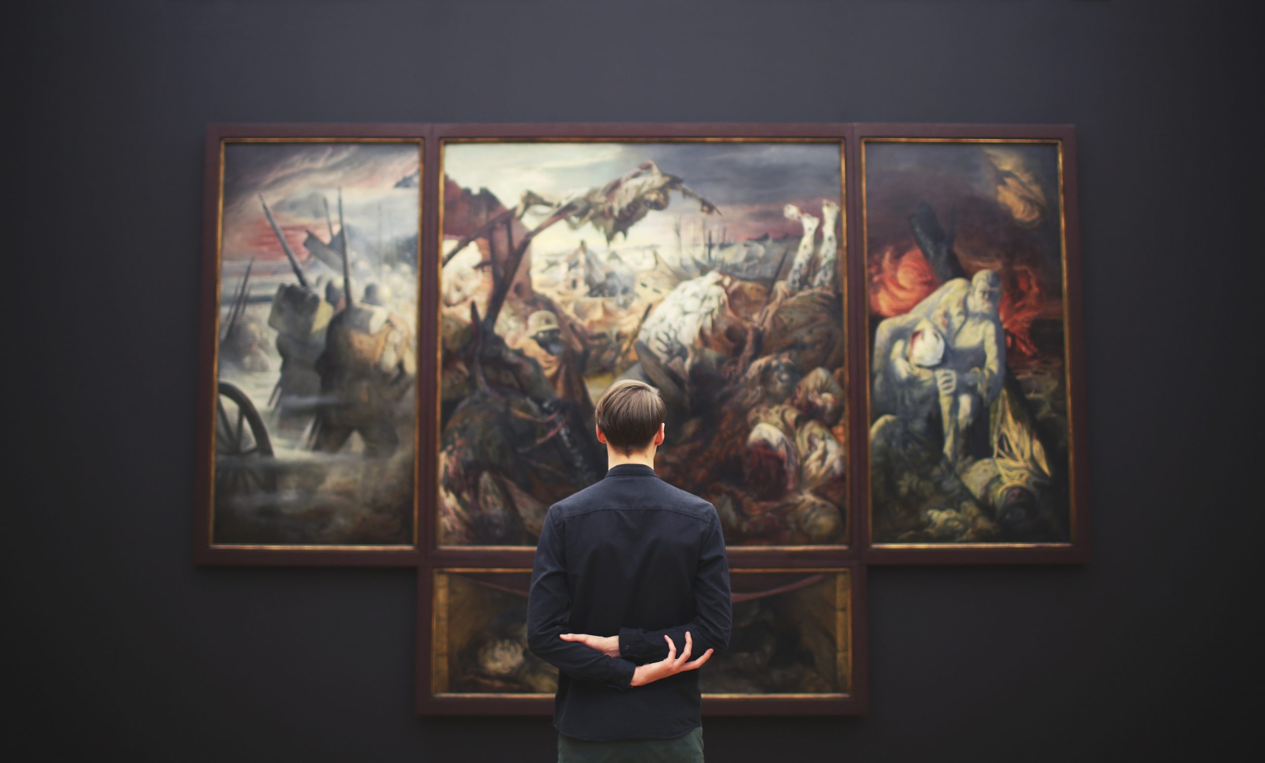 Ein Mann betrachtet ein Gemälde und hält dabei die Arme hinter seinem Rücken zusammen.