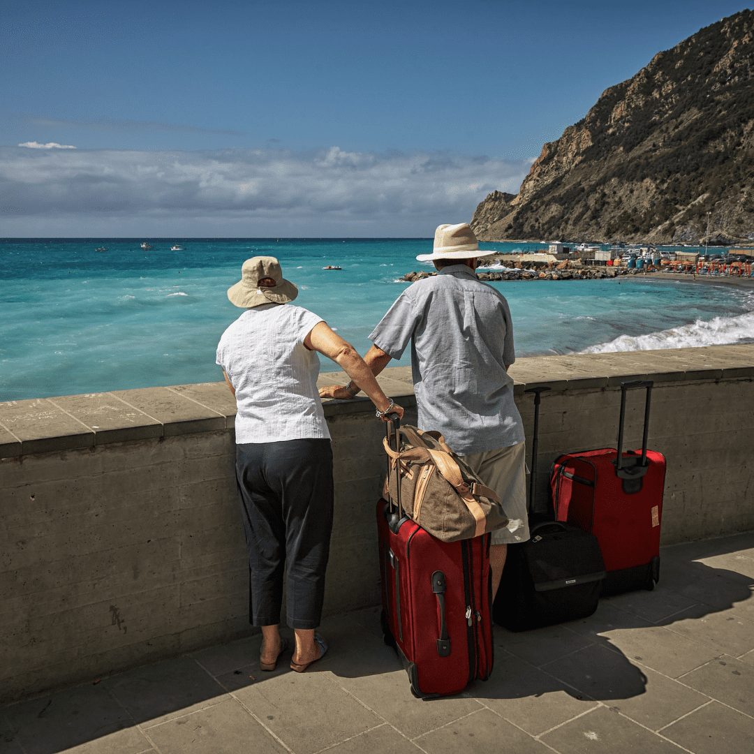 Ein altes Ehepaar mit Koffern blickt aufs Meer.