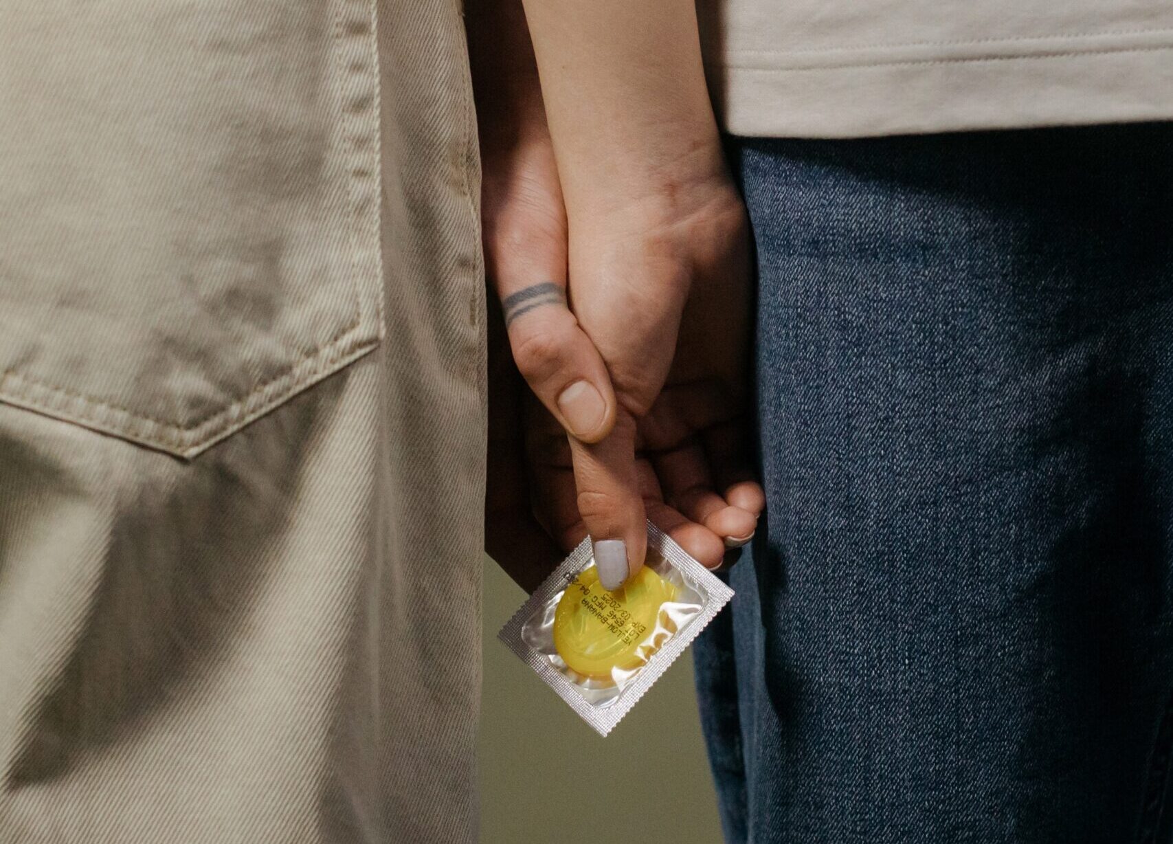 Zwei Menschen halten Händchen. In ihren Händen ist ein Kondom