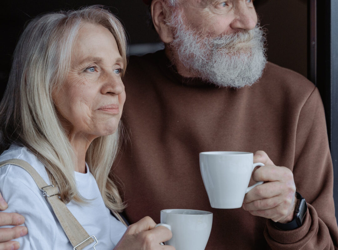 Zwei ältere Menschen, umarmen sich mit Tassen in den Händen