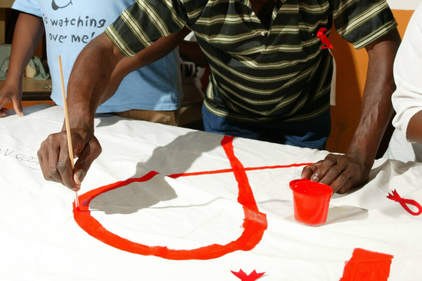 Mann zeichnet eine AIDS-Schleife auf ein Transparent für die Präventionsarbeit in einem AIDS-Hospiz