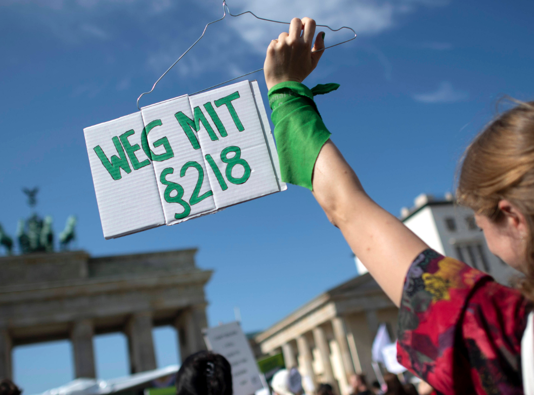 Eine Aktivistin auf einer Demo in Berlin hält vor dem Brandenburger Tor ein Schild hoch, auf dem "Weg mit §218" steht.