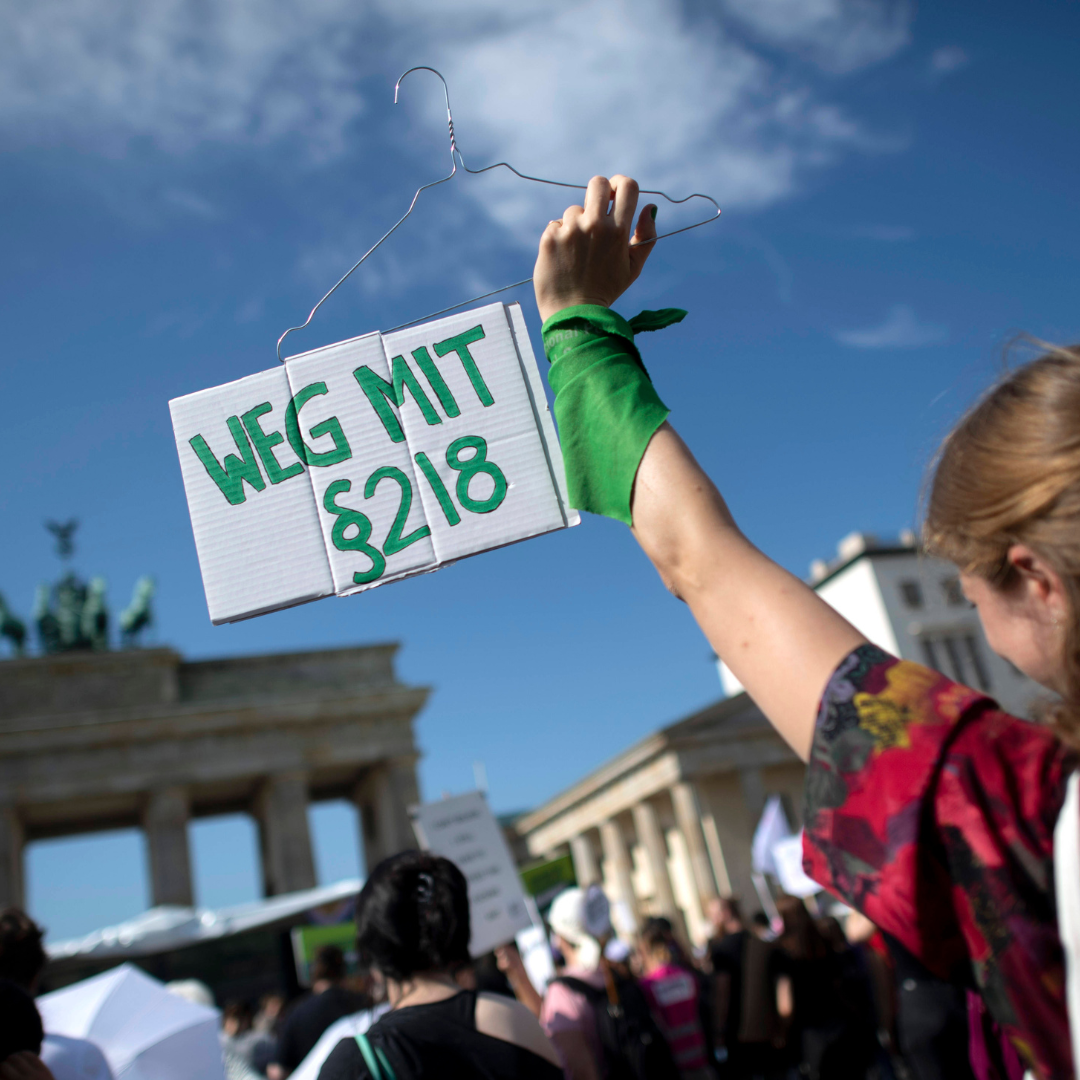 Eine Aktivistin auf einer Demo in Berlin hält vor dem Brandenburger Tor ein Schild hoch, auf dem "Weg mit §218" steht.