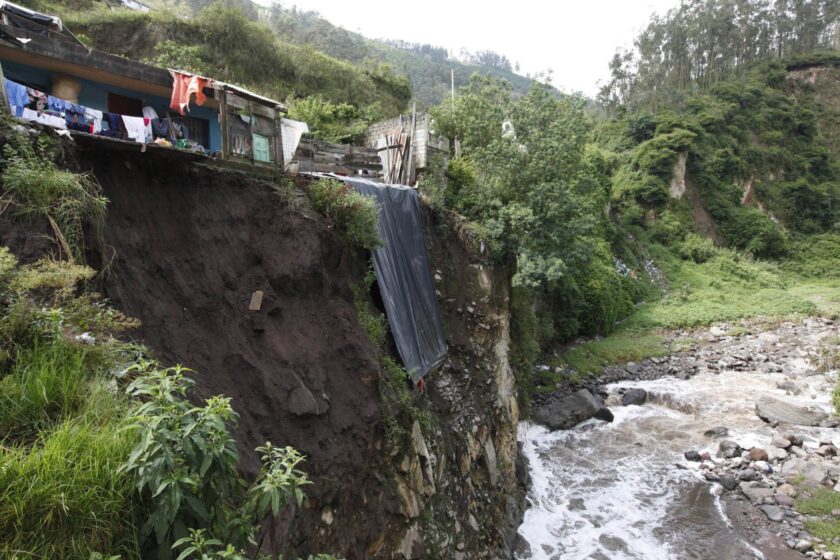 ein Bild des Rio Machangara in der Nähe von Quito, Ecuador. Man sieht einen steilabfallenden Hang, auf dem einige Häuser stehen, darunter der Fluss, der durch eine grüne Landschaft braust.