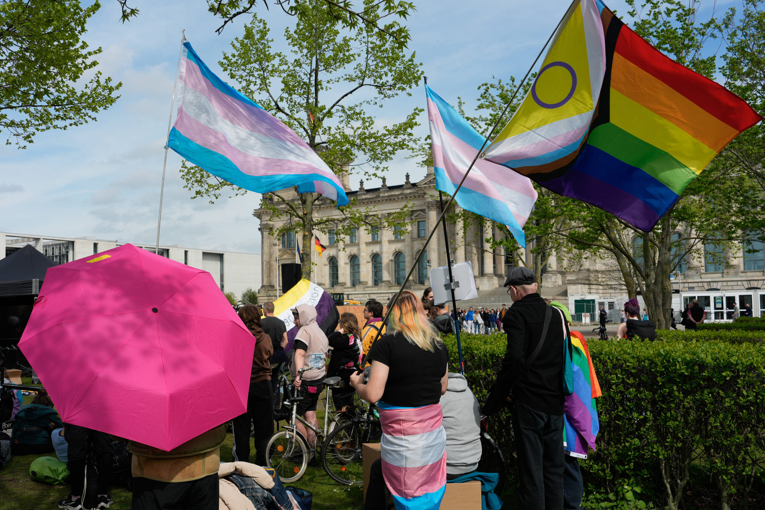 eine Gruppe von Menschen schwenkt progressive Regenbogen- und Transflaggen