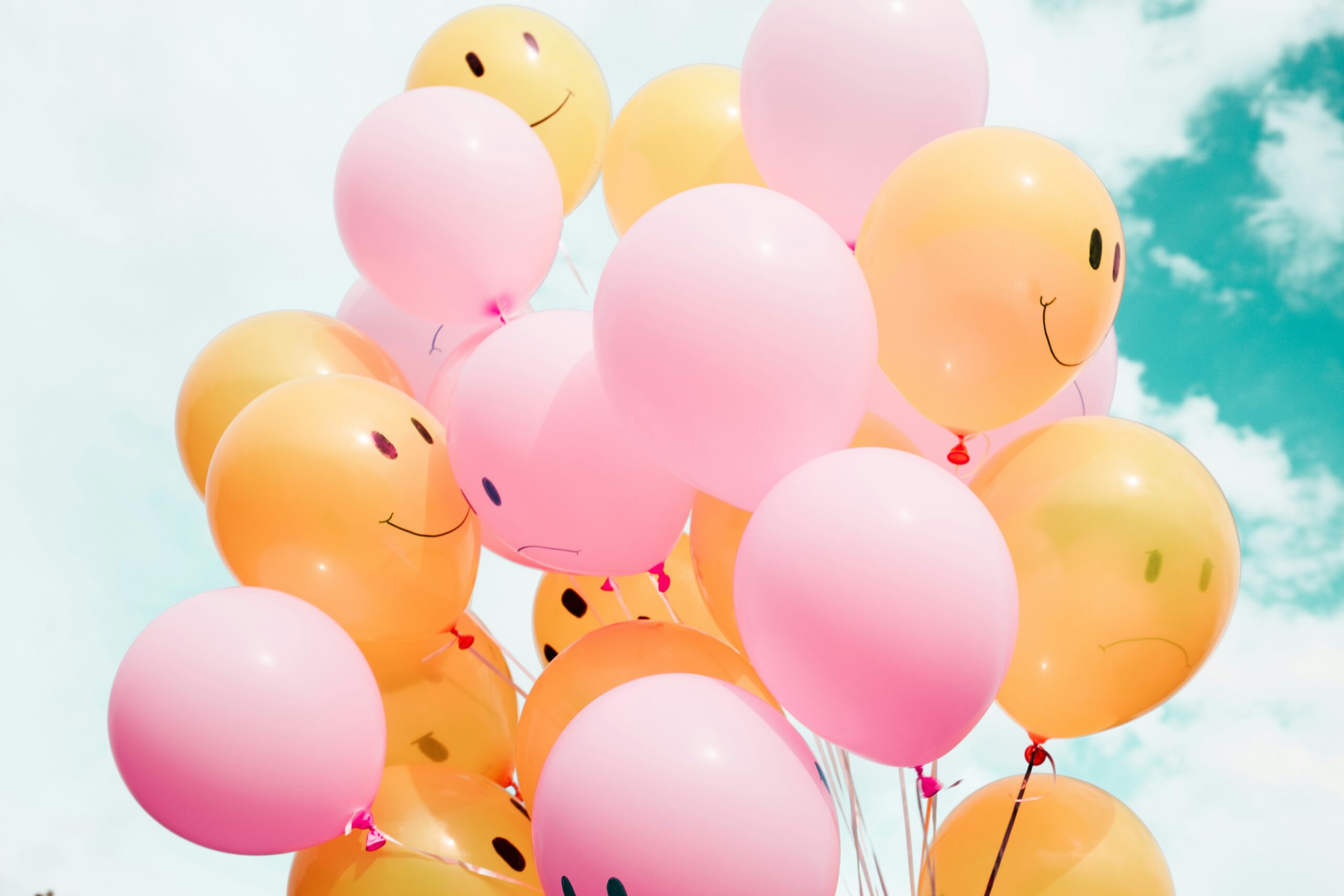 Eine Traube orangefarbener und pinker Luftballons mit Smileygesichtern vor einem blauen Himmel