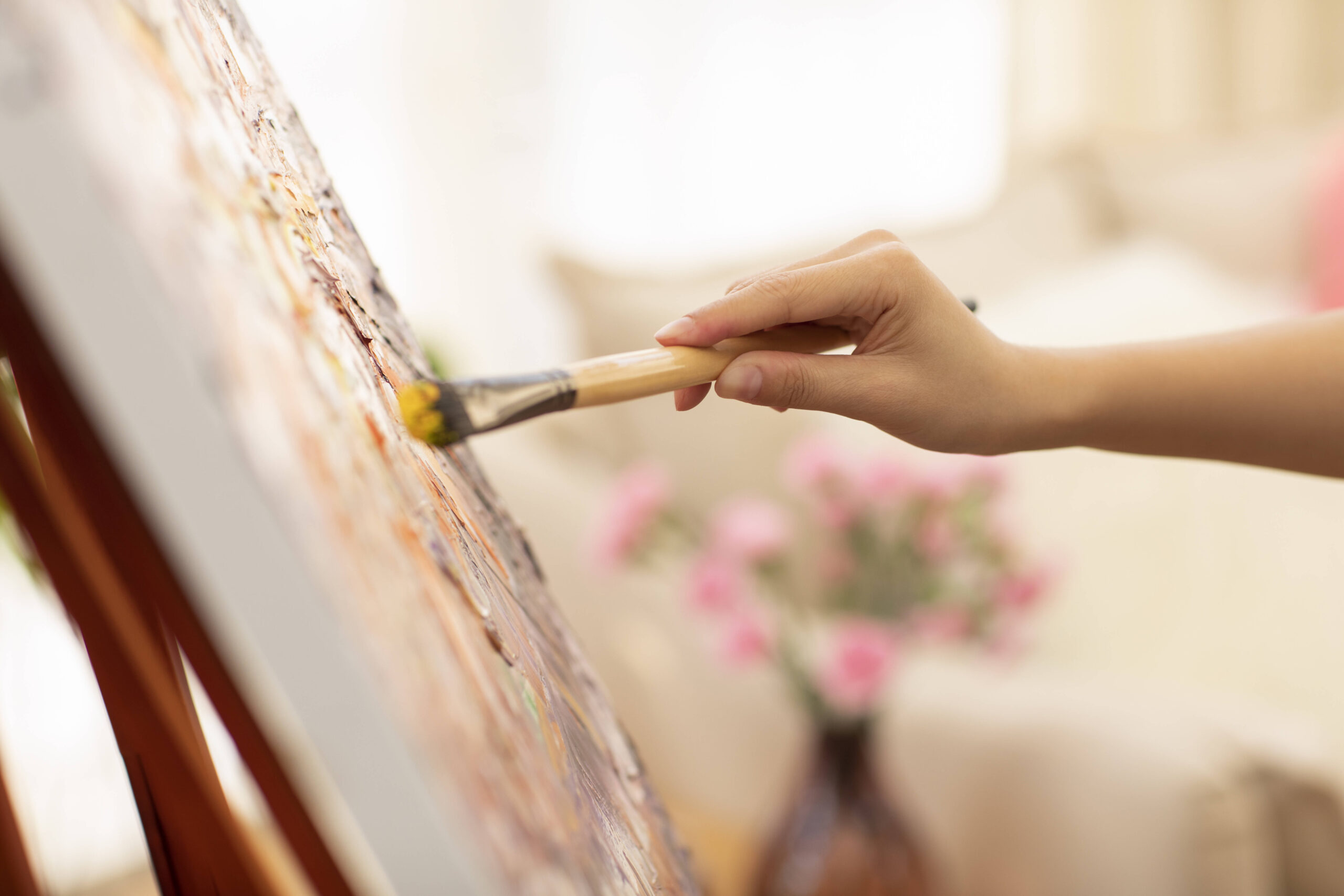 Hand einer Person, die mit Pinsel auf eine Leinwand malt