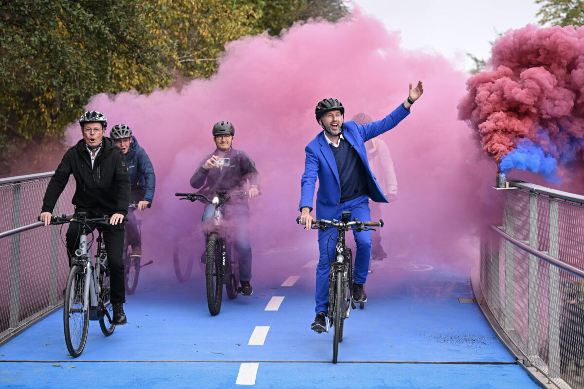 Tübingens Oberbürgermeister Boris Palmer (re) und Regierungspraesident Klaus Tappeser (CDU) fahren zur Eröffnung mit dem Fahrrad über die Tübinger Radbrücke, im Hintergrund pinker dekorativer Rauch