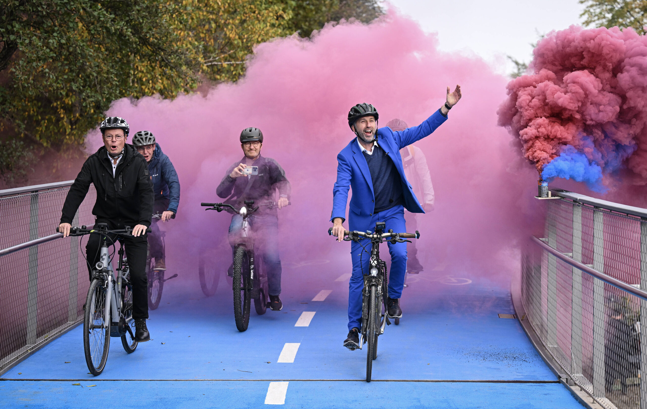 Tübingens Oberbürgermeister Boris Palmer (re) und Regierungspraesident Klaus Tappeser (CDU) fahren zur Eröffnung mit dem Fahrrad über die Tübinger Radbrücke, im Hintergrund pinker dekorativer Rauch