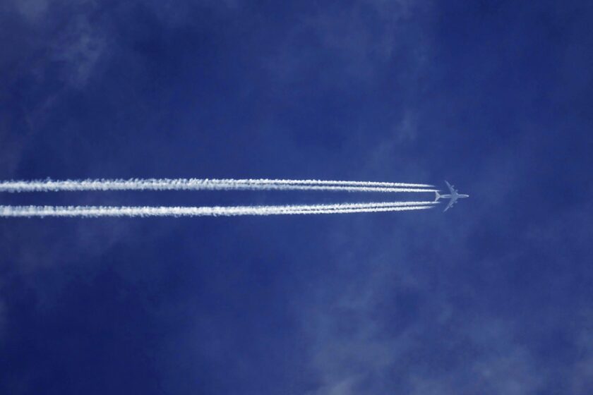 Ein Flugzeug zieht Kondensstreifen über einen azurblauen Himmel