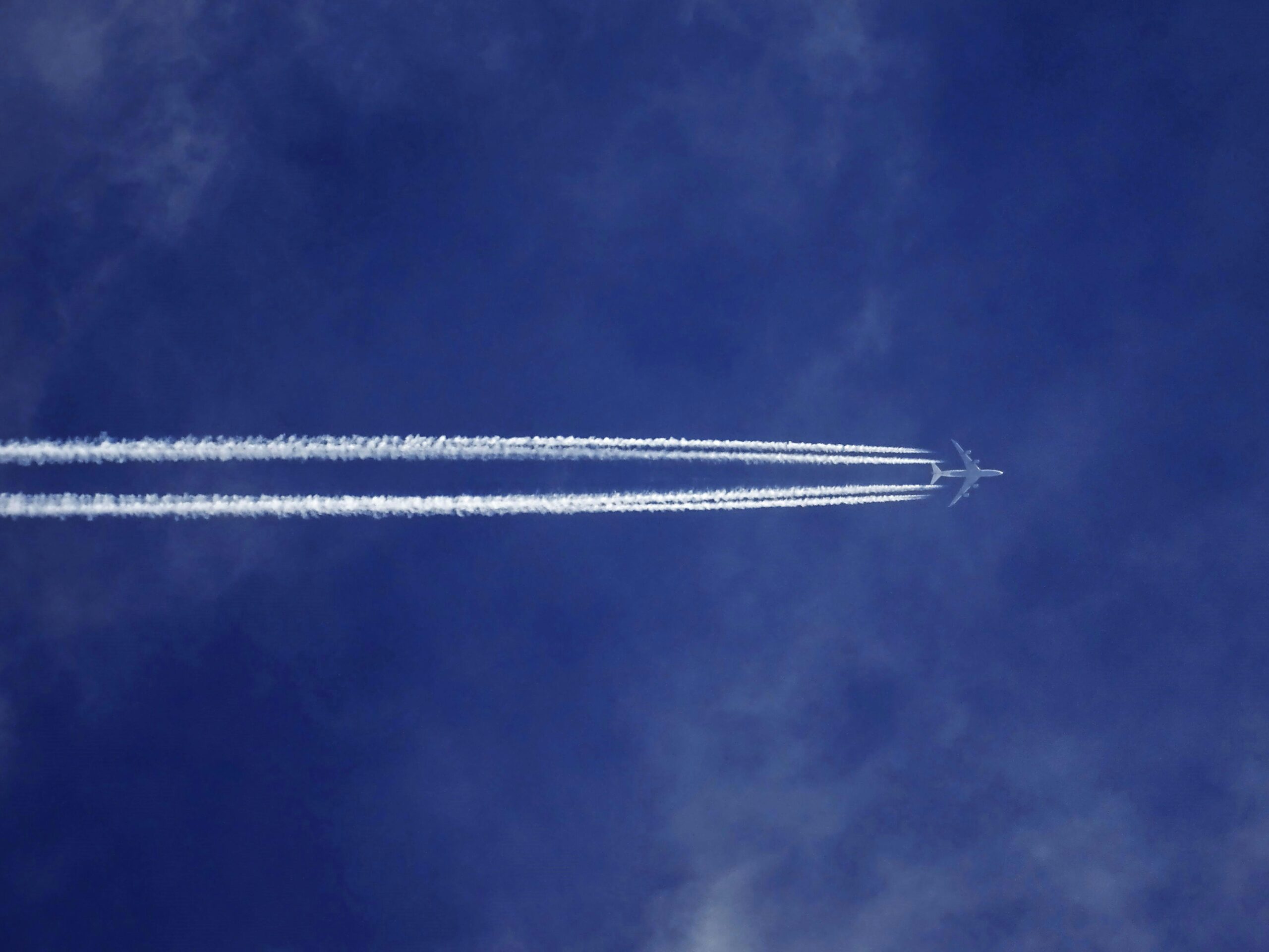 Ein Flugzeug zieht Kondensstreifen über einen azurblauen Himmel