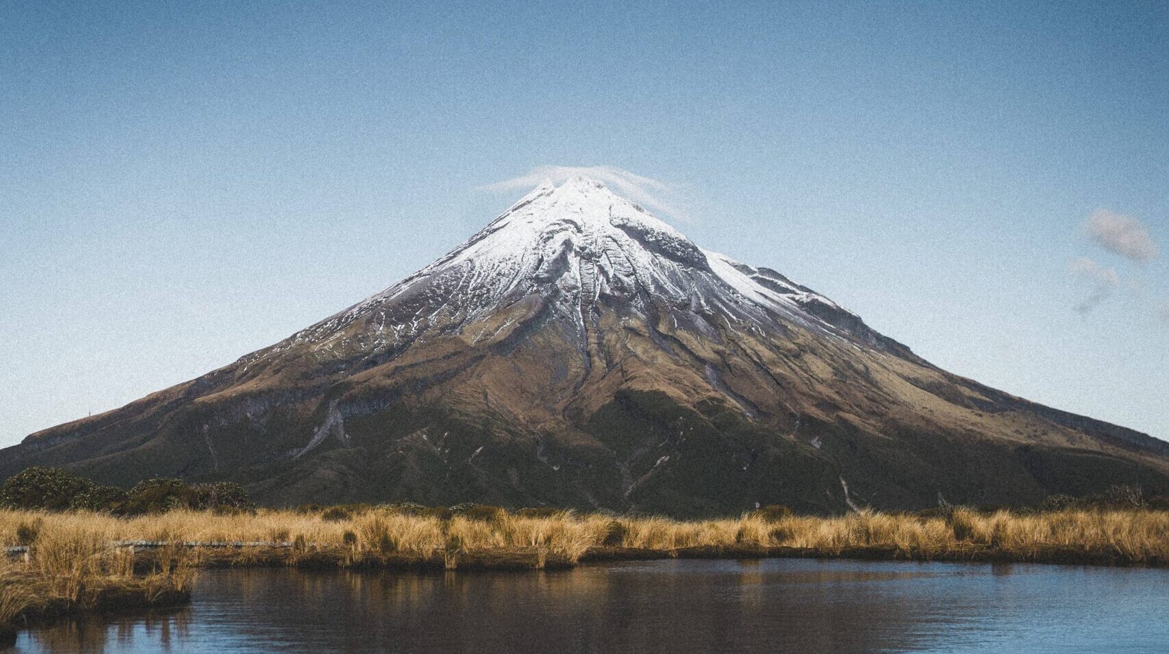 Ein schneebedeckter Berg spiegelt sich in einem stillen See unter einem klaren blauen Himmel, Mount Taranaki,