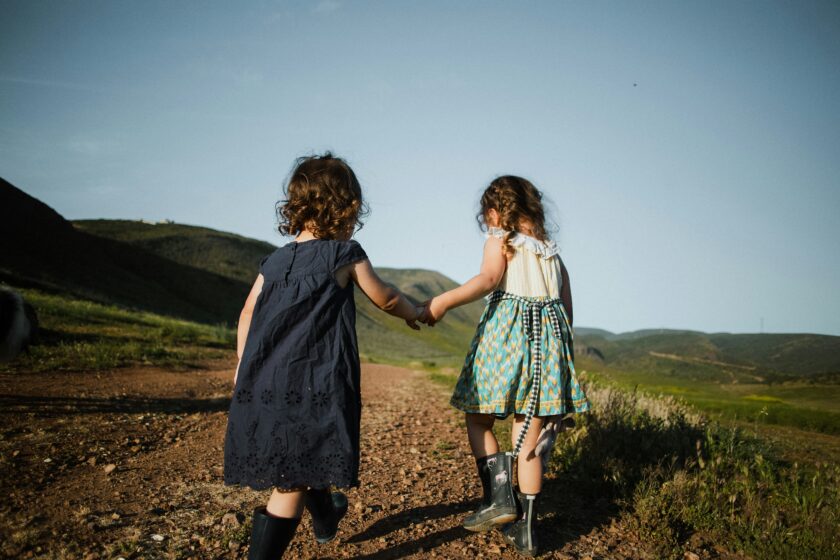 Zwei Mädchen laufen Hand in Hand über eine Wiese