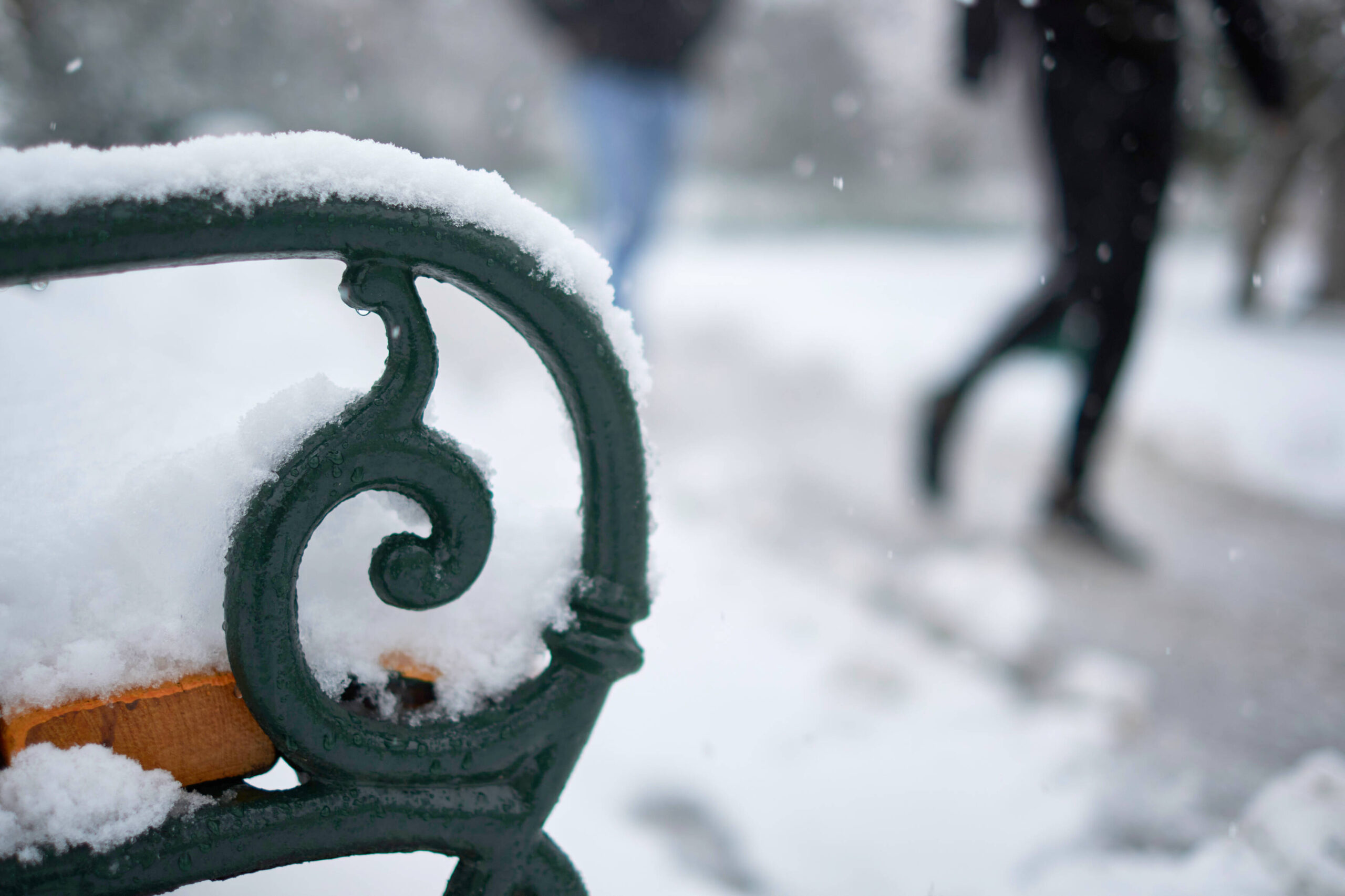 Verschneite Parkbank im Stadtpark mit vorbeigehenden Menschen