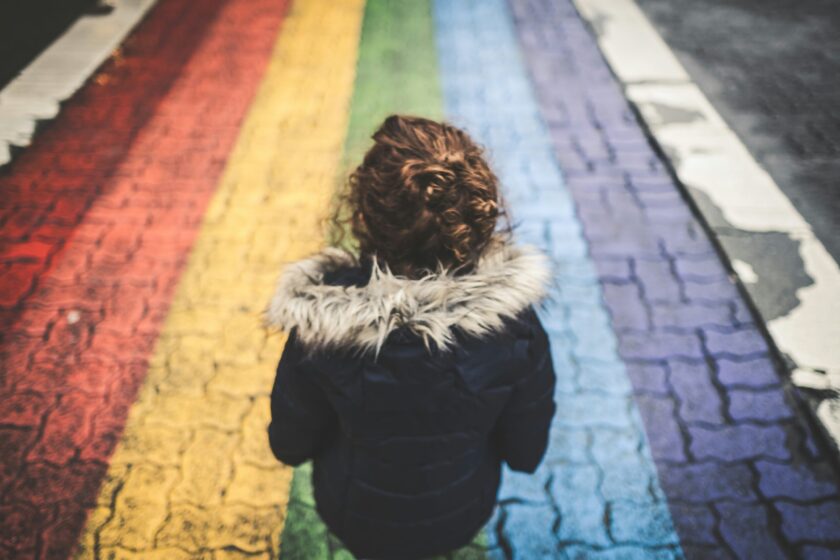 Kind steht vor einer Kopfsteinstraße, auf die ein Regenbogen gemalt ist